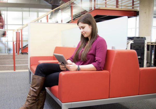 Young woman sitting in an orange chair reading. 